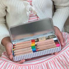 a person holding a tin with colored pencils in it