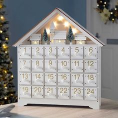 a white wooden house shaped calendar sitting on top of a table next to a christmas tree