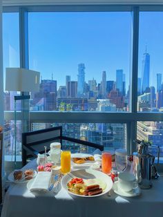 a table topped with plates of food next to a window filled with cityscape