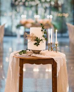 a wedding cake sitting on top of a wooden table next to two candles and greenery