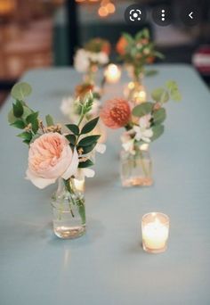 several vases with flowers are sitting on a table next to some candles and lights