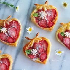 four heart shaped pastries with strawberries and daisies on a marble counter top