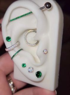 a person holding an earring and ring in their hand with green jewels on it