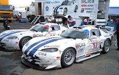 three race cars parked next to each other in front of a semi truck and trailer