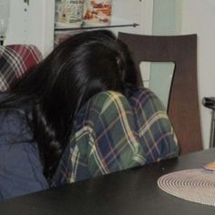 a woman sitting at a table with her head on the back of a chair looking down