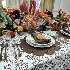 a table set for thanksgiving dinner with pumpkins, flowers and other autumn decorations on it