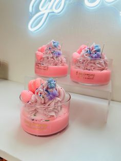 three small cakes with pink frosting and sprinkles on them sitting in front of a neon sign