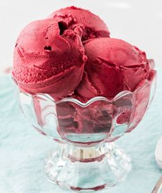 three scoops of red ice cream in a glass bowl on a blue tablecloth