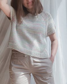 a woman standing in front of a window with her hands on her head and wearing silver pants