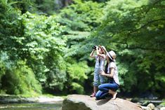 two people are sitting on a rock by the river and taking pictures with their cell phones stock photo