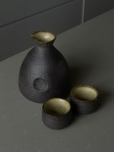 three black vases sitting next to each other on a gray counter top with white tiles in the background