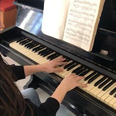 a woman sitting at a piano playing an organ with sheet music on the top shelf