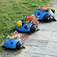 three blue ladybug planters with flowers in them sitting on the side of a road