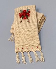 a knitted scarf with red flowers and tassels on the ends is laying on a gray surface