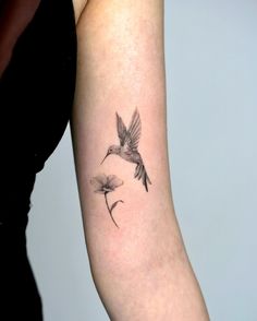 a woman's arm with a small tattoo of a hummingbird and dandelion