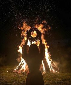 a person standing in front of a fire pit with their hands up to the sky