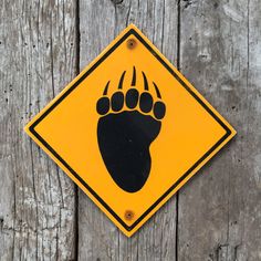 a yellow and black bear paw crossing sign on a wooden fence with wood planks