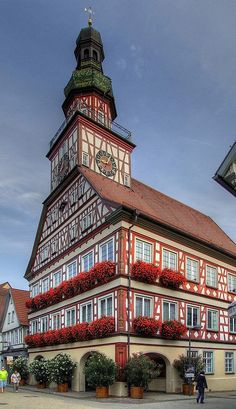 an old building with red flowers on the windows and balconies in front of it