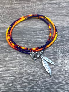 the multicolored beaded bracelet has two silver charms and a feather charm on it