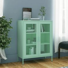 a green cabinet sitting in front of a window next to a chair and potted plant