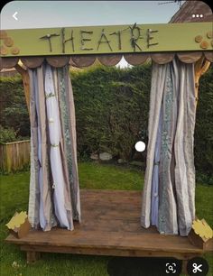 an outdoor stage with curtains and the word theatre on it's side, in front of a garden