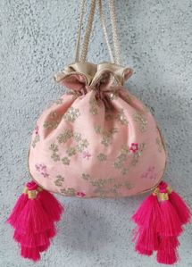 a pink purse hanging on the wall with two tassels and a gold bow