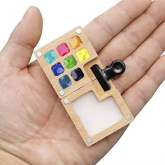 a hand holding a small wooden toy with different colors on it's side and an object in the middle that is shaped like a house