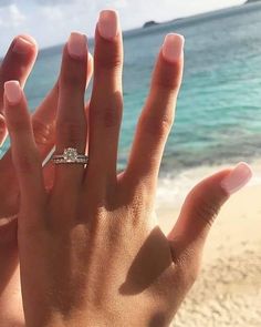 a woman's hand on the beach with her engagement ring in their left hand