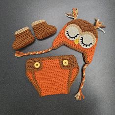 a crocheted owl hat, diaper cover and booties are on the table