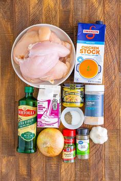 ingredients to make chicken broth laid out on a wooden table with an apple, onion, garlic, and seasoning