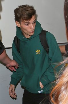 a young man wearing a green sweatshirt and carrying a black backpack walks through an airport