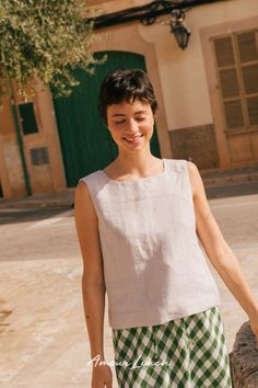 a woman standing in front of a building with her hands in her pockets and smiling at the camera