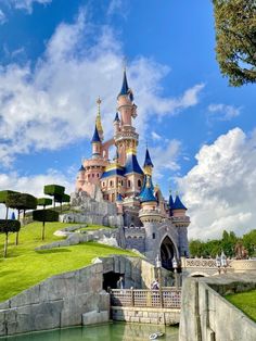 the castle is built on top of a hill and surrounded by green grass, with people walking around it