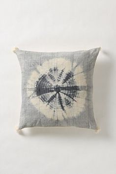 a gray and white pillow with a tie - dyed design on the front, sitting against a white wall