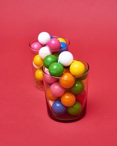 two clear cups filled with colorful candies on a pink surface