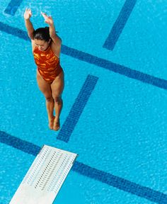 a woman in an orange swimsuit jumping into a pool with her hands up to the side