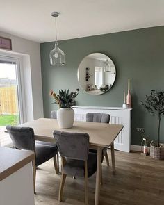 a dining room table with grey chairs and a round mirror on the wall above it