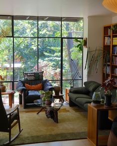 a living room filled with furniture next to a window covered in lots of greenery