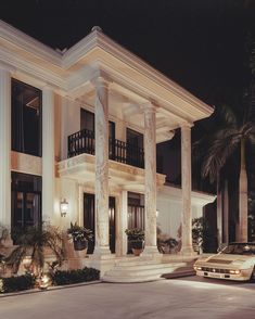 a car is parked in front of a large house at night with columns and pillars