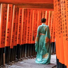 a woman in a green kimono standing next to rows of orange and black columns