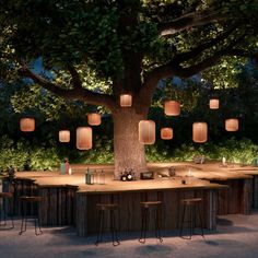 an outdoor bar with lanterns hanging from the tree and lights on the wall above it