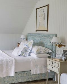 a bed with white sheets and pillows in a bedroom next to a painting on the wall