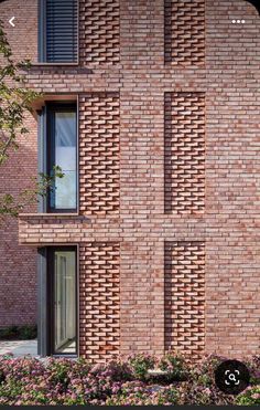 a brick building with several windows and flowers in the foreground on a sunny day