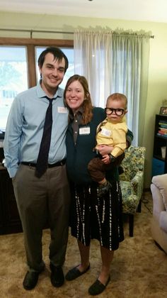 a man standing next to a woman holding a baby in her arms and smiling at the camera