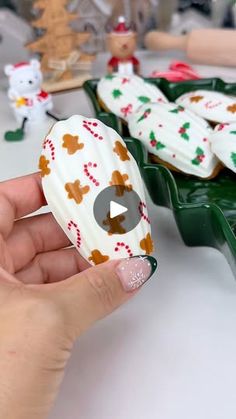 a person is holding some cookies in front of other decorated cookies on trays with christmas decorations around them