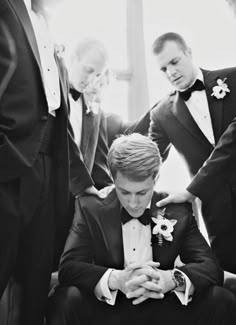 a black and white photo of a man in a tuxedo looking at his phone