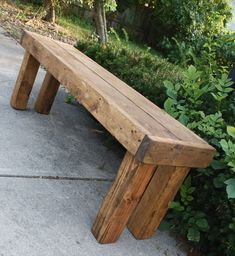 a wooden bench sitting on top of a cement ground next to bushes and trees in the background