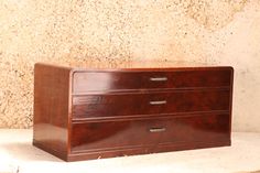 a brown wooden dresser sitting on top of a white floor next to a stone wall