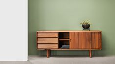 a small potted plant sitting on top of a wooden cabinet next to a green wall