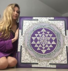 a woman kneeling down next to a purple and white art piece on a wooden table